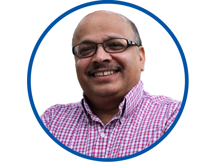 Circular headshot of Tilak Chandra with a blue border. Tilak has dark skin, brown eyes, glasses, and a moustache,, and is wearing a red and white checked shirt.