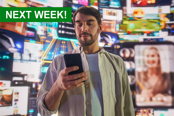 Young man with a beard looking at his cell phone in front of a colorful social media wall of screens.