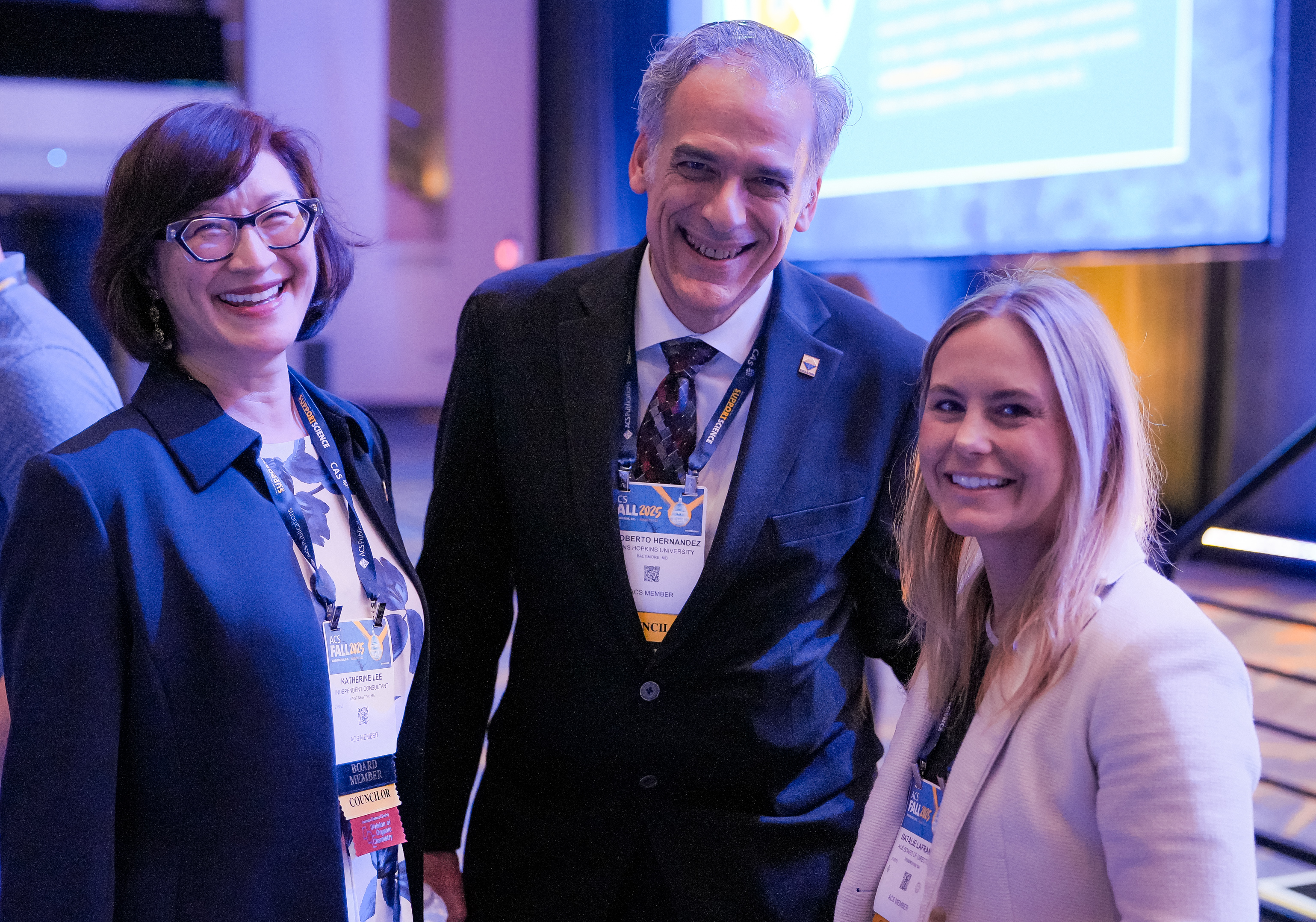 Three attendees, a man and two women, smile at an ACS Fall 2025 event.